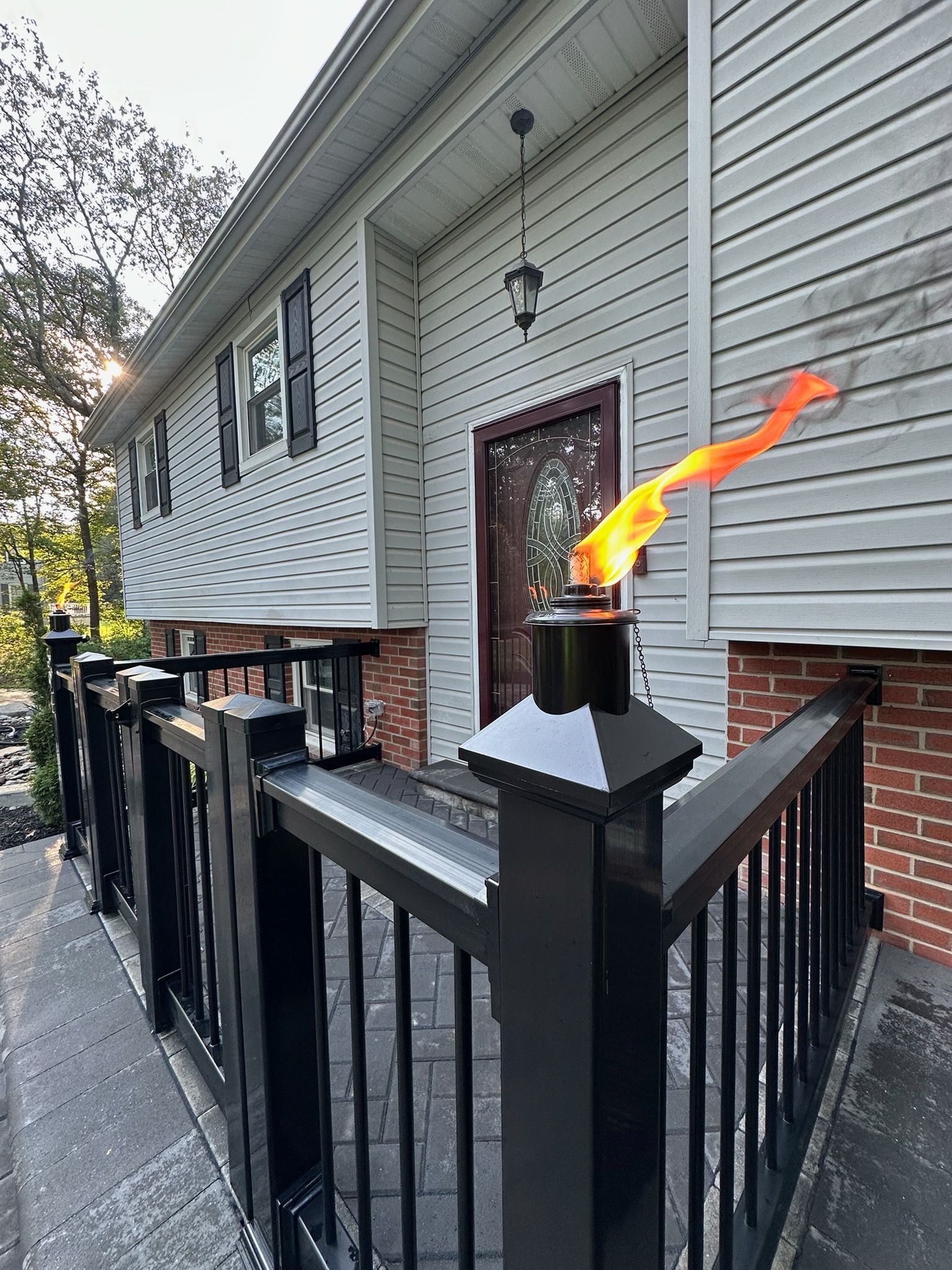 Front porch with a black metal railing and a flaming torch beside a gray house entryway