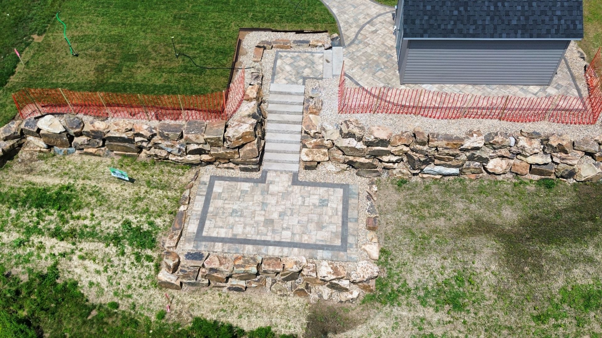 Stone patio and retaining wall beside a house, with a tiled square platform in a grassy yard.