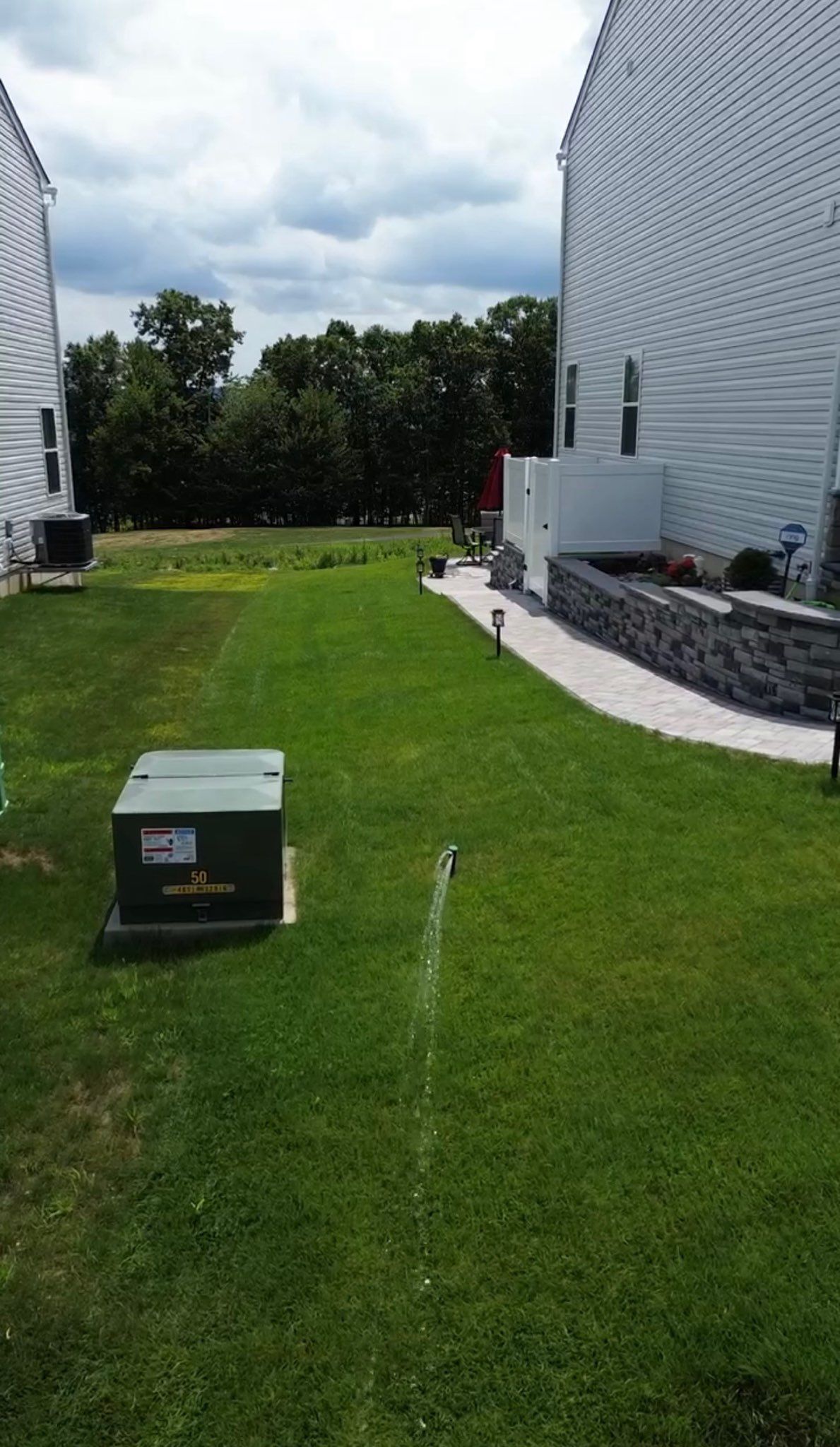 Grassy path between two modern white buildings, with a small box in the foreground and trees beyond.