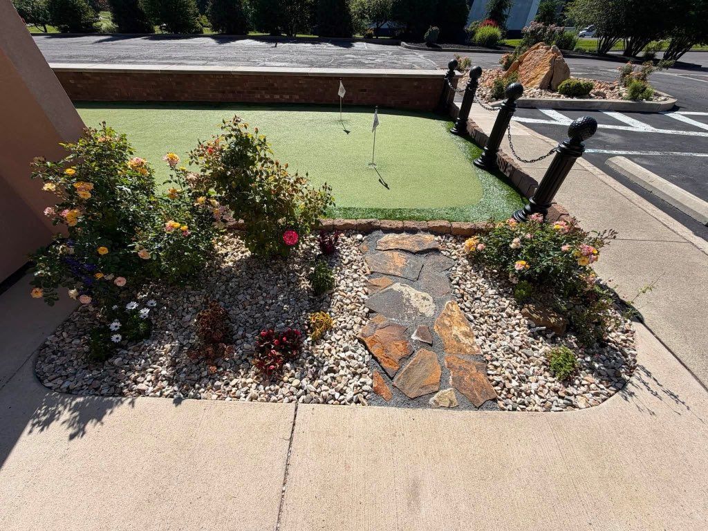 Front yard xeriscape with rocks, flowers, and a small green pond or fountain beside a sidewalk