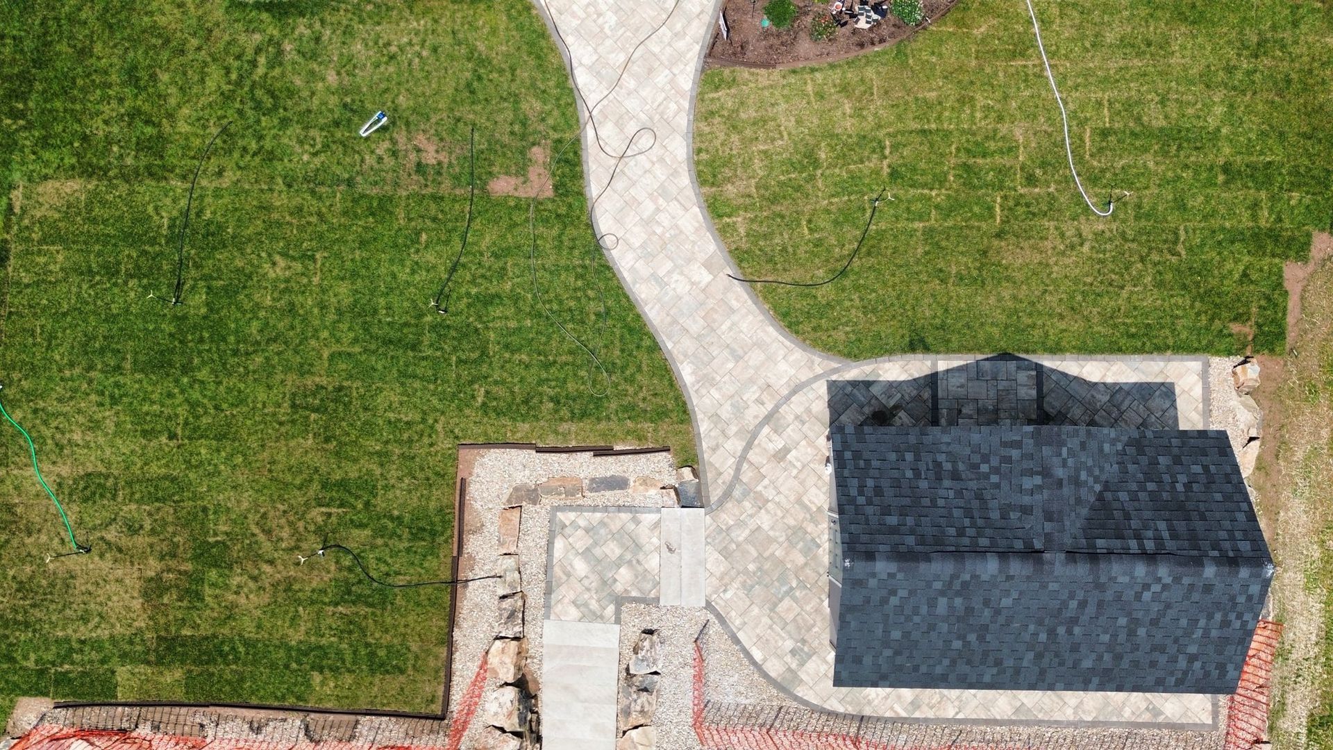 Aerial view of a grassy yard with a curved stone path and a paved patio beside a dark-roofed structure