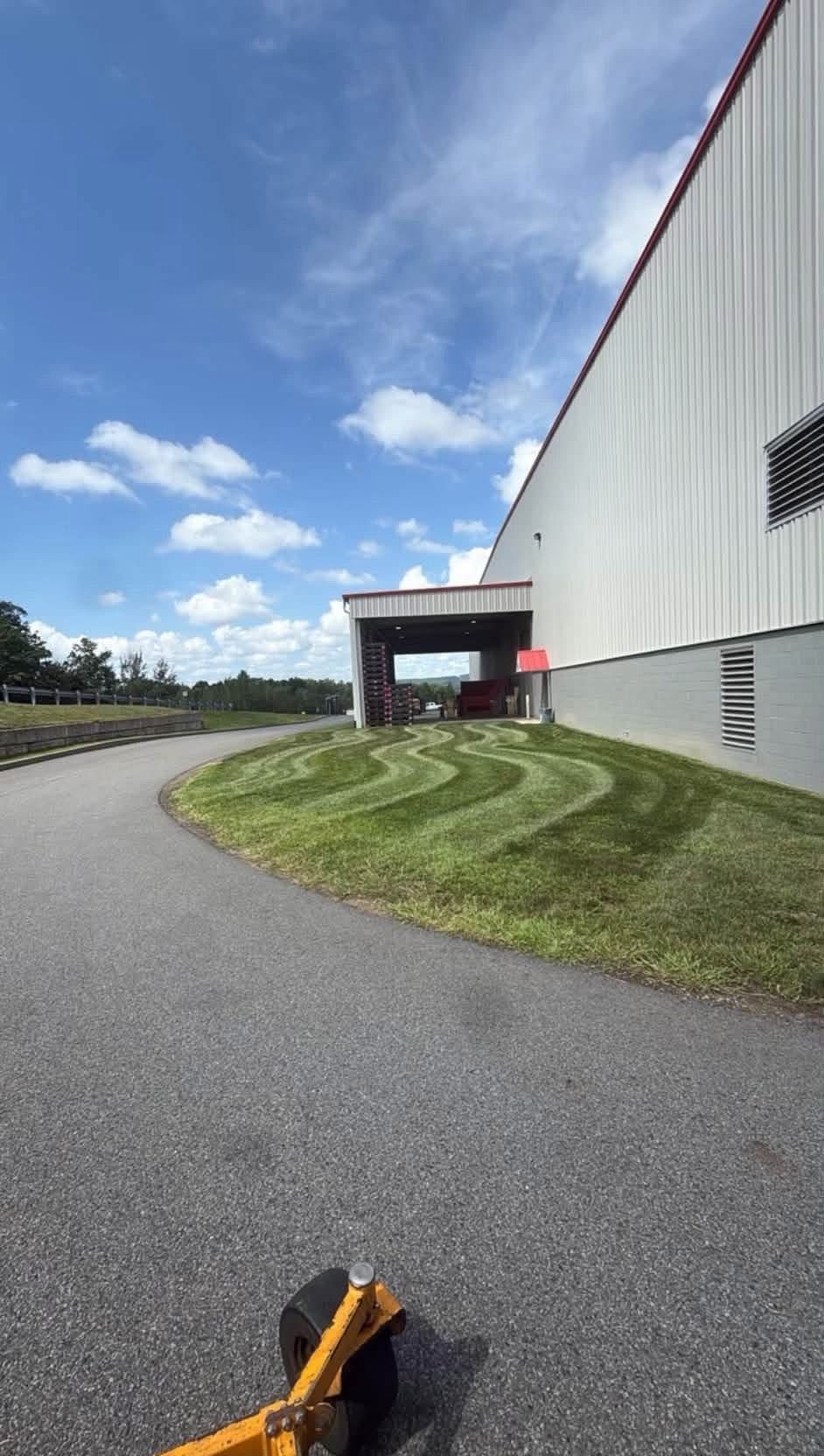 Curving gravel path beside a corrugated metal building under a blue sky with clouds