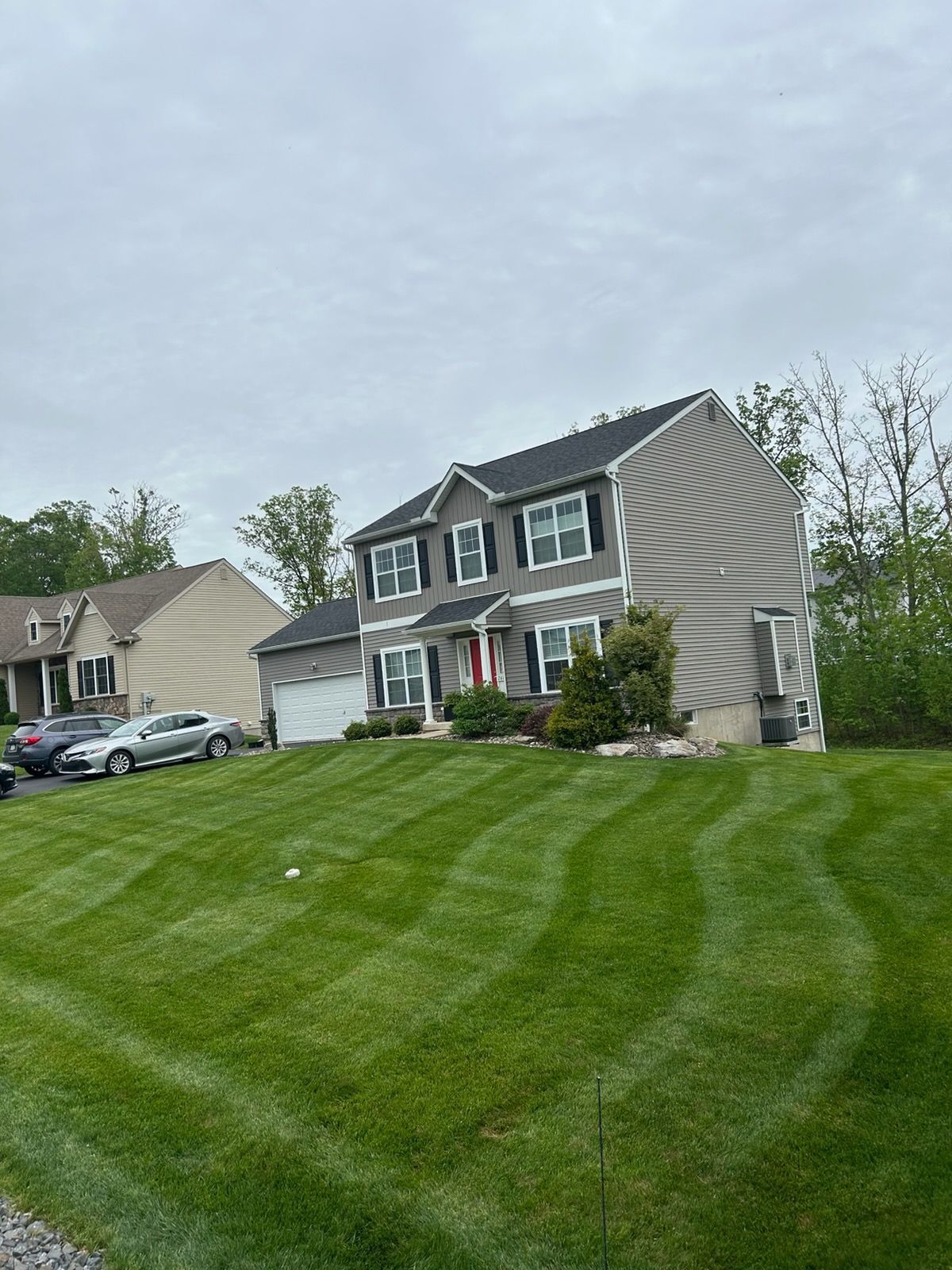 Suburban house with gray siding and striped green lawn under an overcast sky