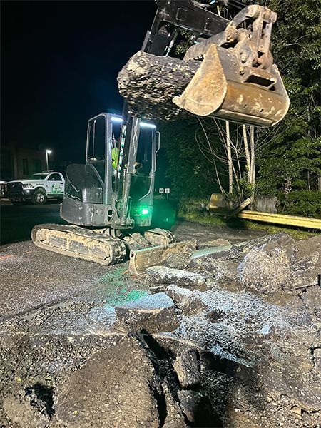 Mini excavator scooping up asphalt at night.