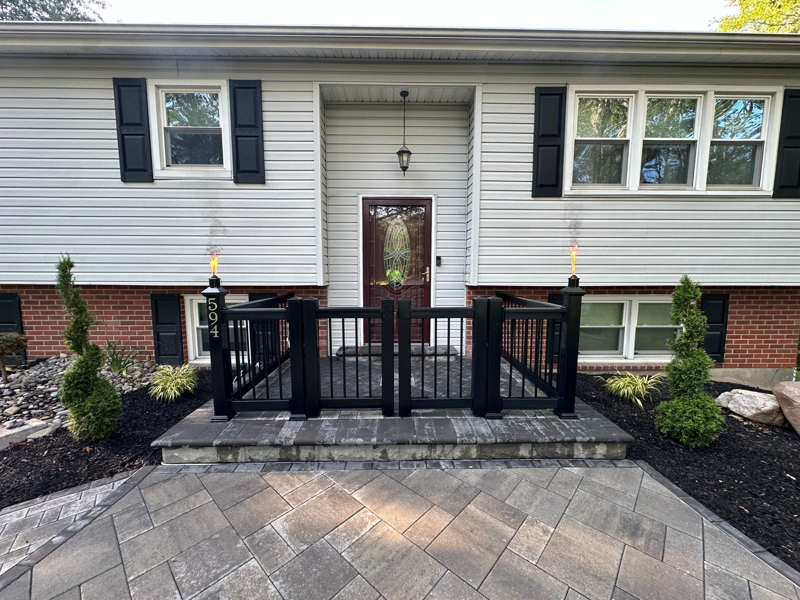 Front entrance of a house with black railings, brick steps, and a tan brick and siding exterior.