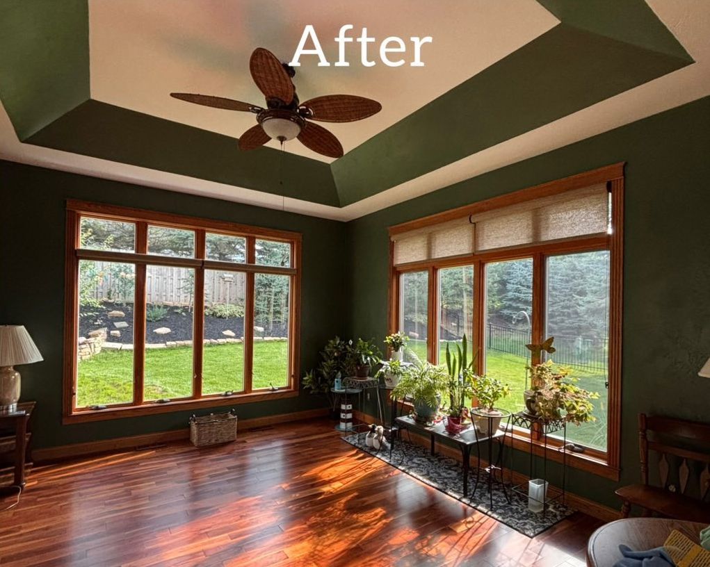 A room with tan walls, wood trim, large windows, a desk, and a ceiling fan. - after