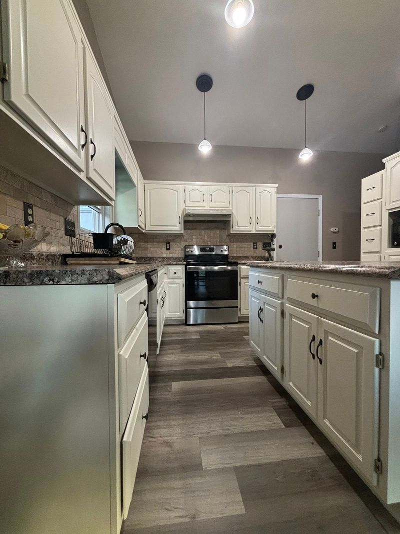 White kitchen with cabinets, island, stainless steel appliances, and pendant lights.