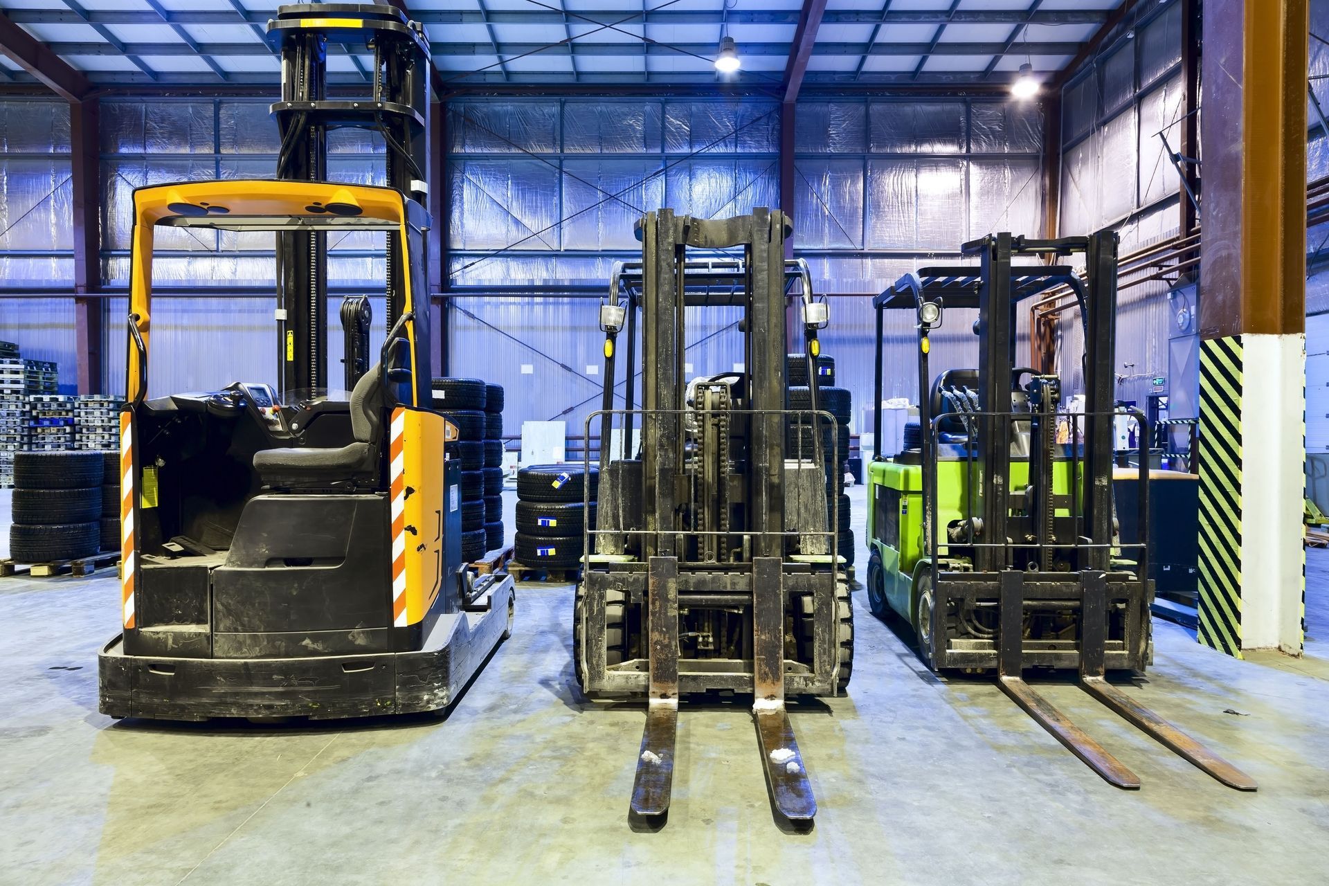 Three forklifts inside a warehouse: yellow, black, and green.
