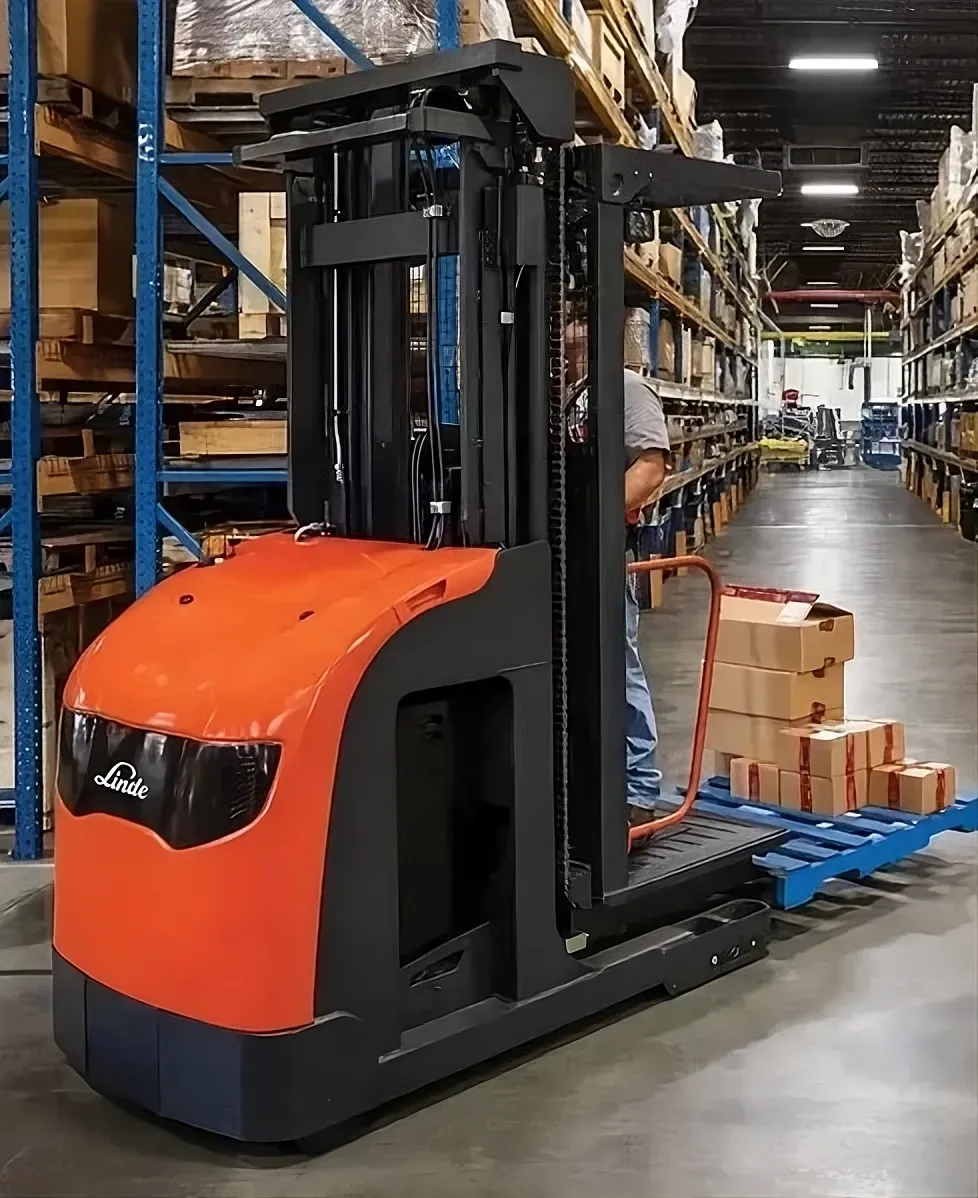 Man operating a forklift in a warehouse aisle with stacked inventory and pallets nearby