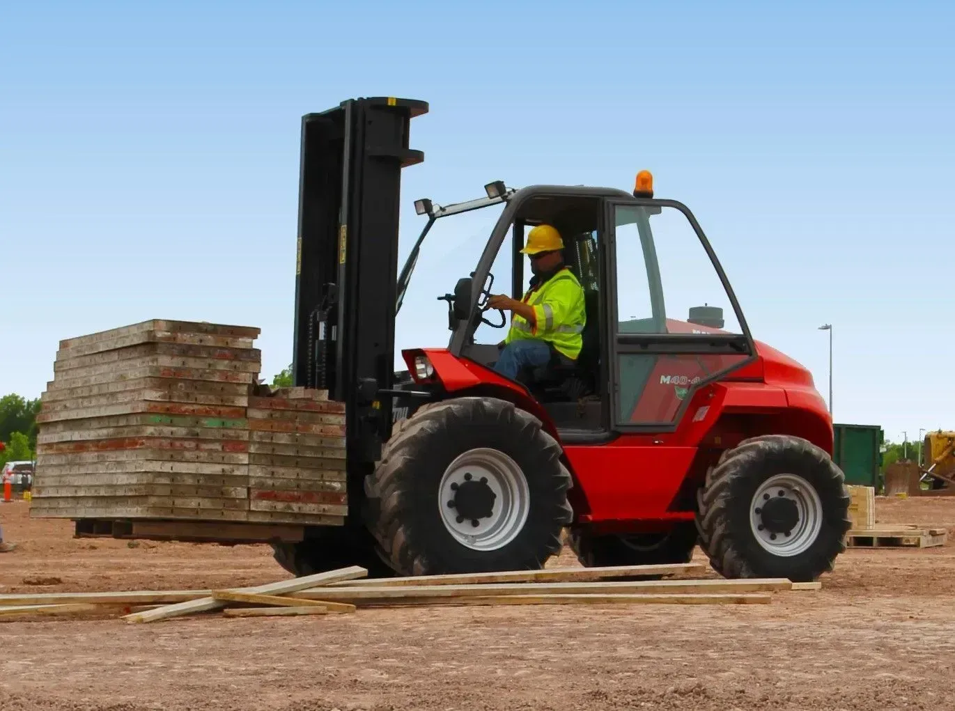 Red forklift lifting stacked wood pallets at an outdoor worksite