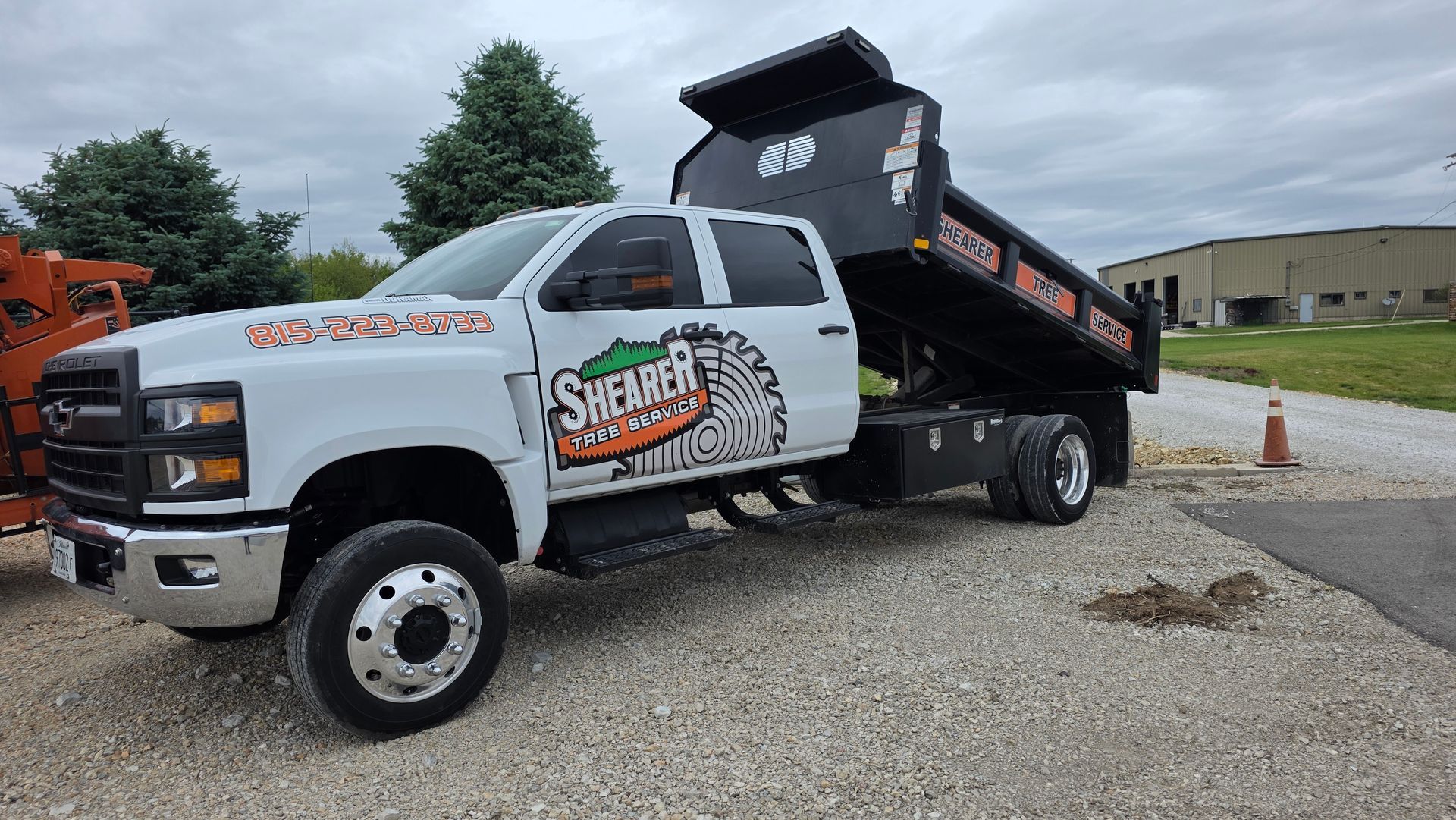 White dump truck with raised black bed and company logo, parked on gravel near a building.