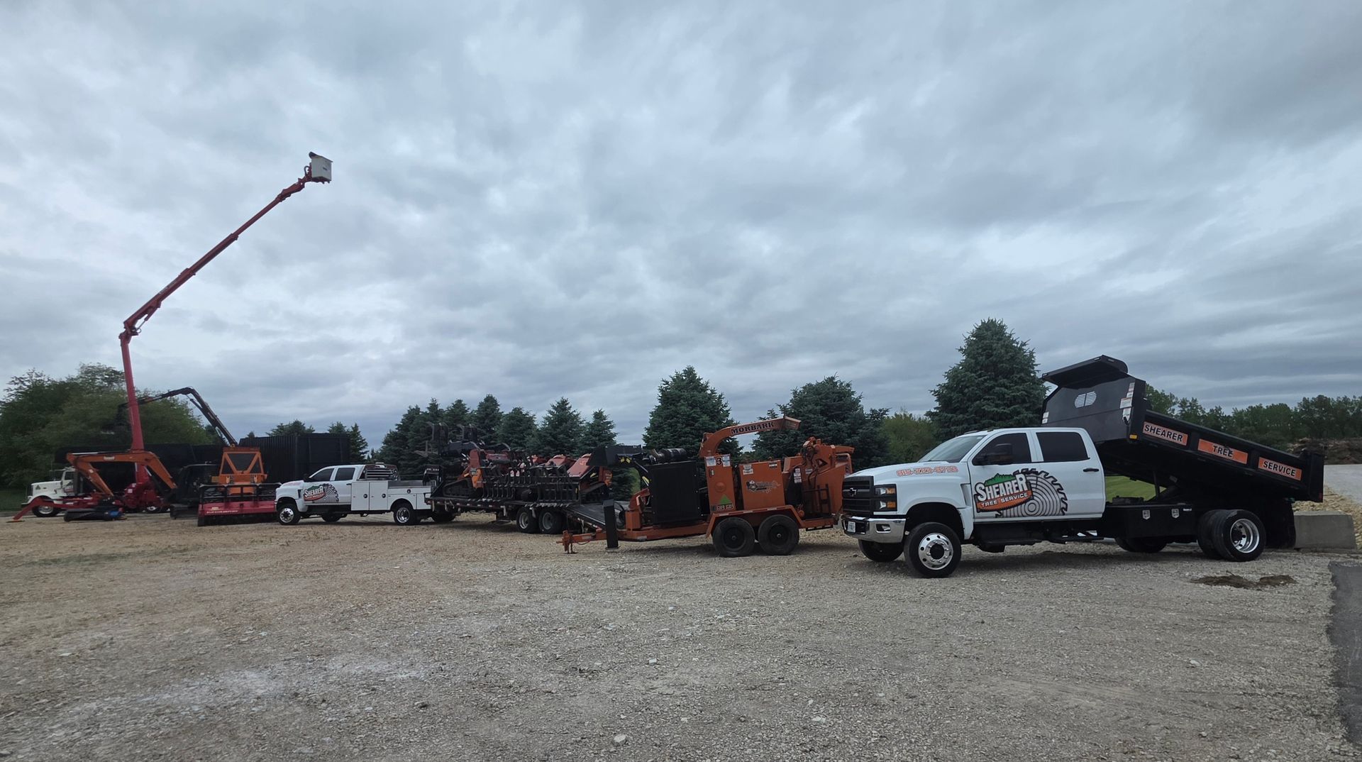Tow trucks and work trucks lined up on a gravel lot under a cloudy sky.