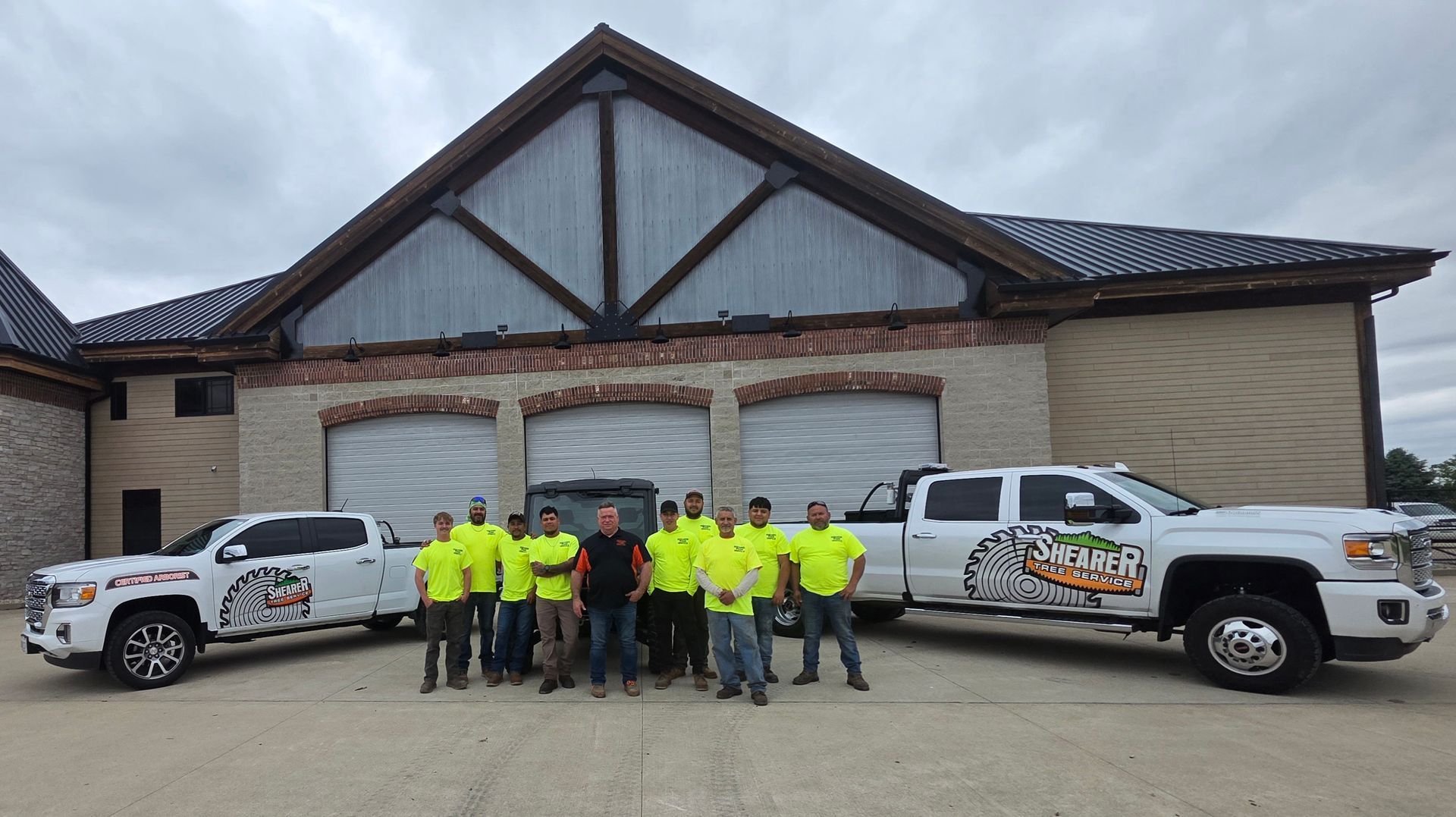 Construction crew in neon shirts posing in front of a house with two work trucks.