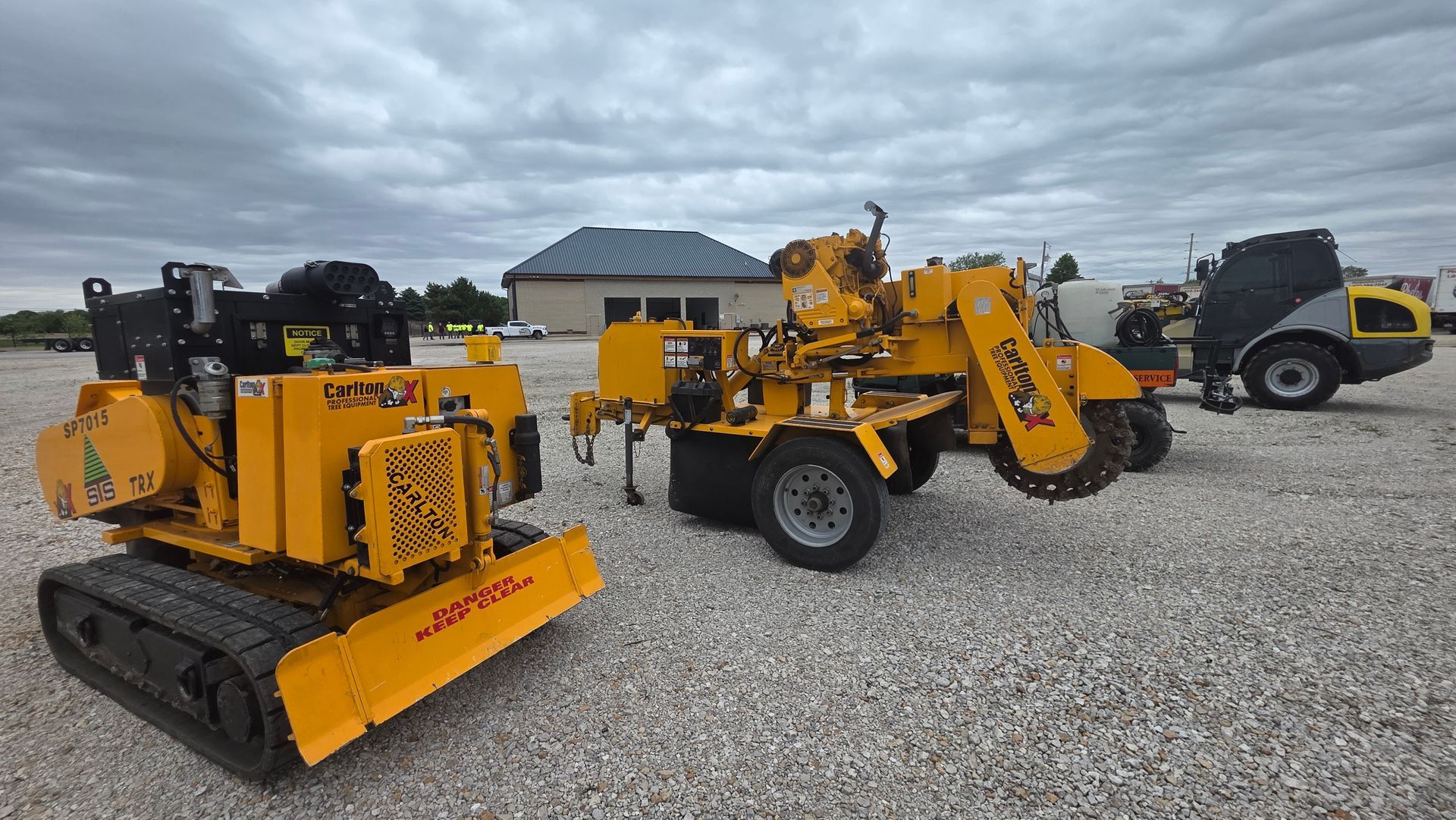 Yellow utility vehicles parked on gravel lot under cloudy sky