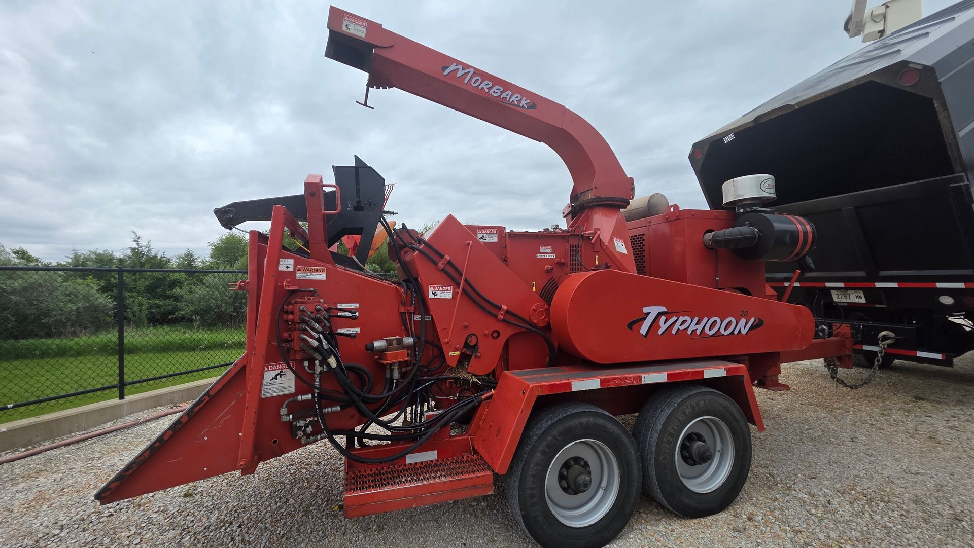 Red wood chipper trailer with red crane attachment parked on gravel beside a field