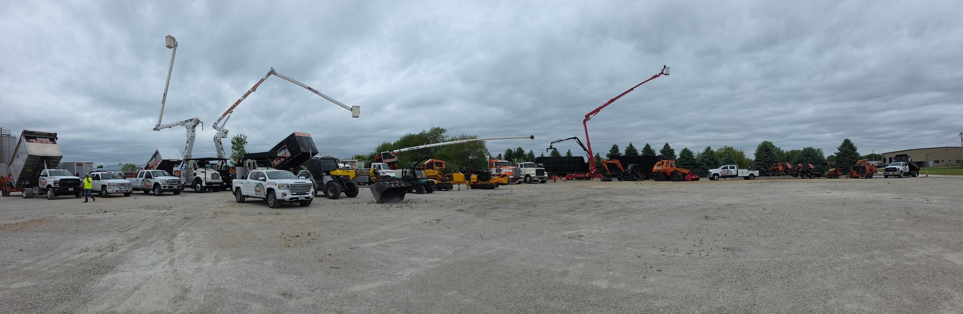 Construction site with cranes, trucks, and equipment on a gravel lot under an overcast sky
