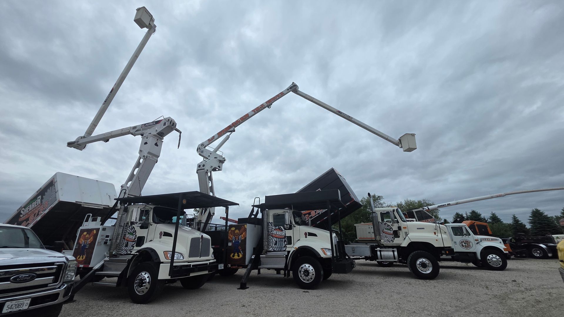 Utility trucks with extended bucket lifts parked in a lot under a cloudy sky