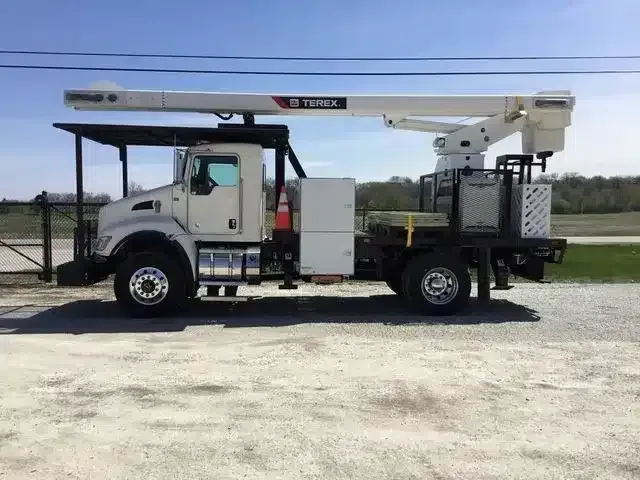 A white Terex utility bucket truck parked on a gravel lot under a clear sky.