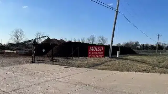 A large pile of dark mulch sits behind a red sign that reads 