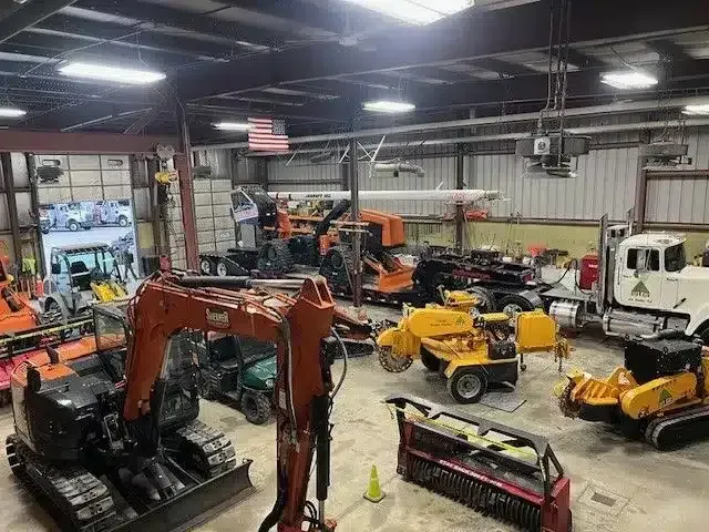 An overhead view of a warehouse filled with construction equipment, including excavators, a dump truck, and machinery.