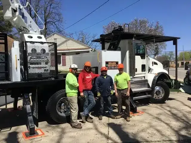 Four people in hard hats and high-visibility gear stand beside a utility truck on a sunny day.