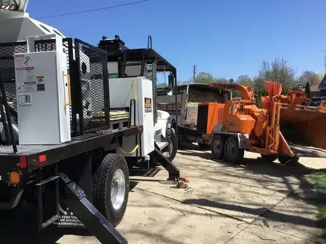 A work truck and a large orange wood chipper parked on a residential driveway on a sunny day.