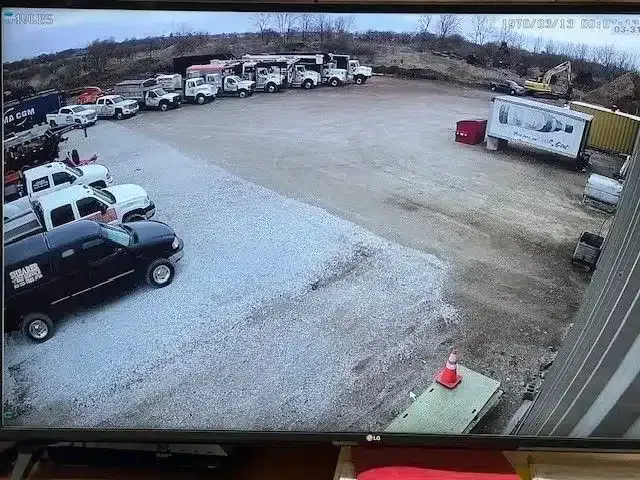 Security footage of a gravel lot filled with parked work trucks and trailers, viewed from an elevated angle.