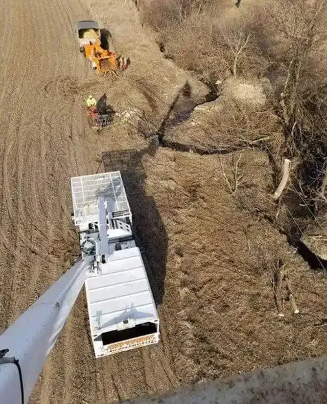 Aerial view of a white utility truck with an extended boom operating near construction workers and earthmoving equipment.