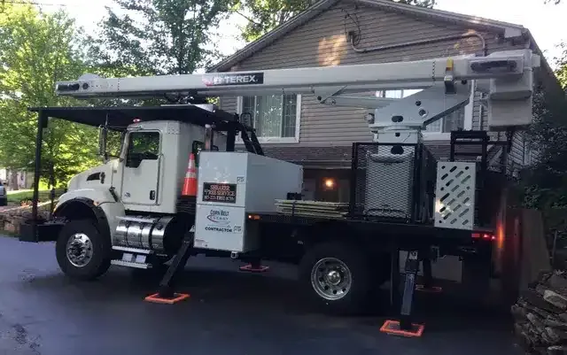 A white utility bucket truck with an extended boom parked on a driveway in front of a residential house.