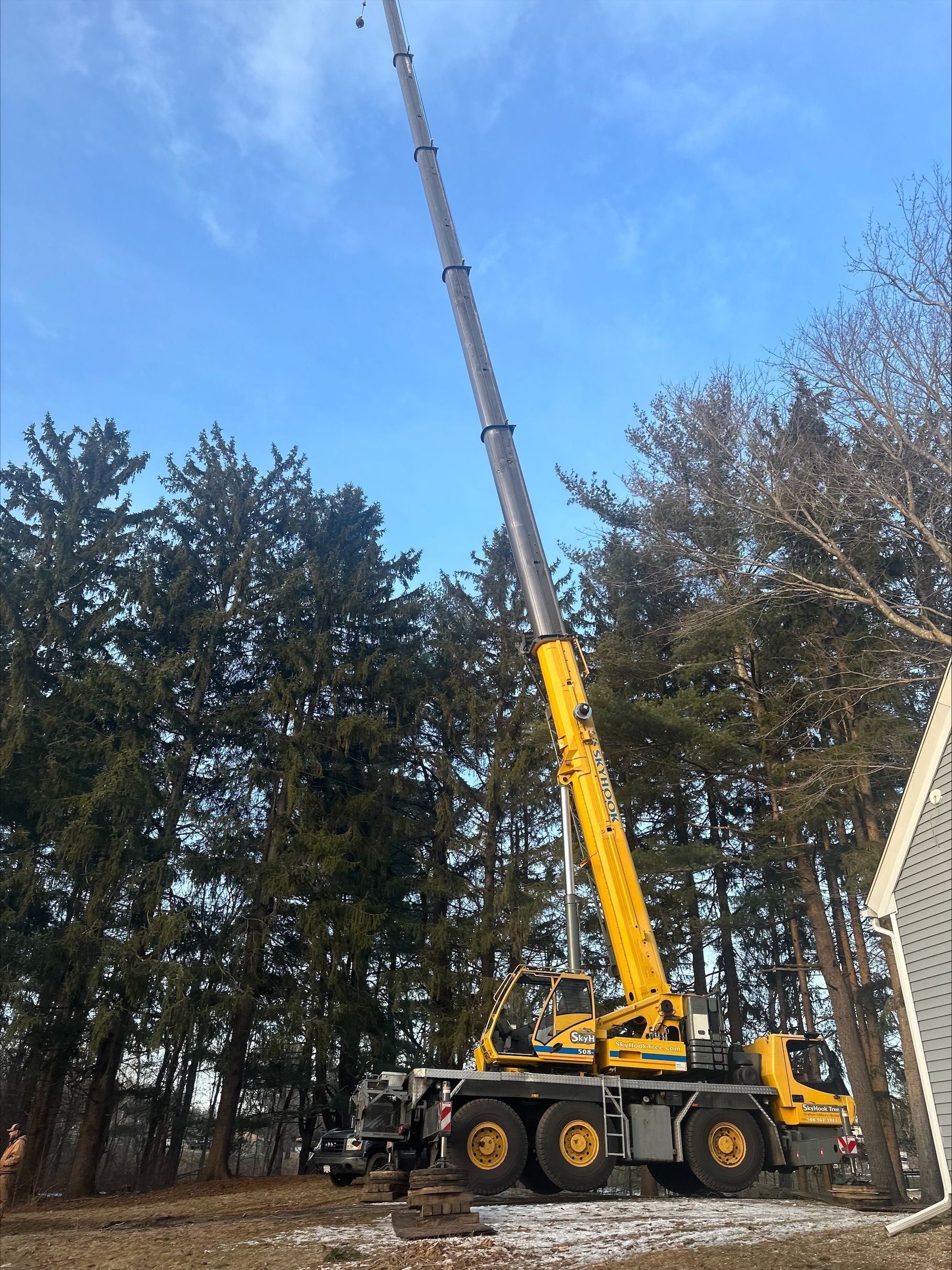 A large yellow crane is parked in front of a house in the woods.
