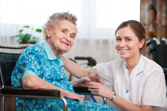 Caregiver smiling while checking an elderly patient’s arm in a wheelchair