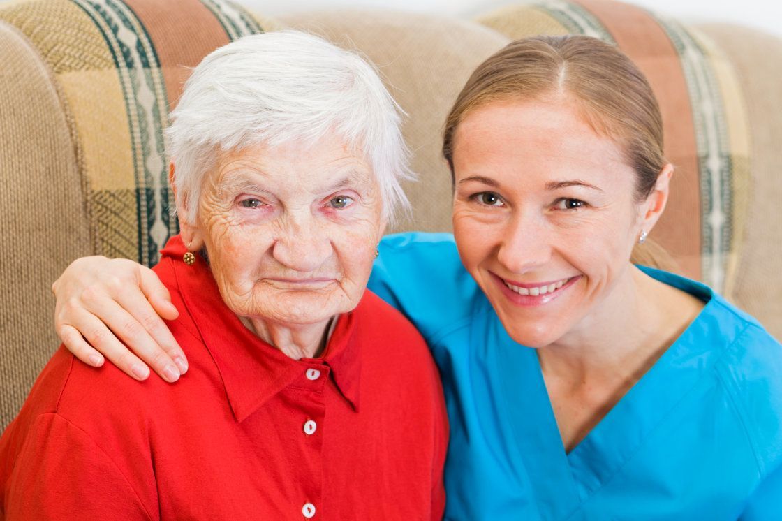 Two smiling people seated together on a couch, one in a red shirt and one in blue scrubs