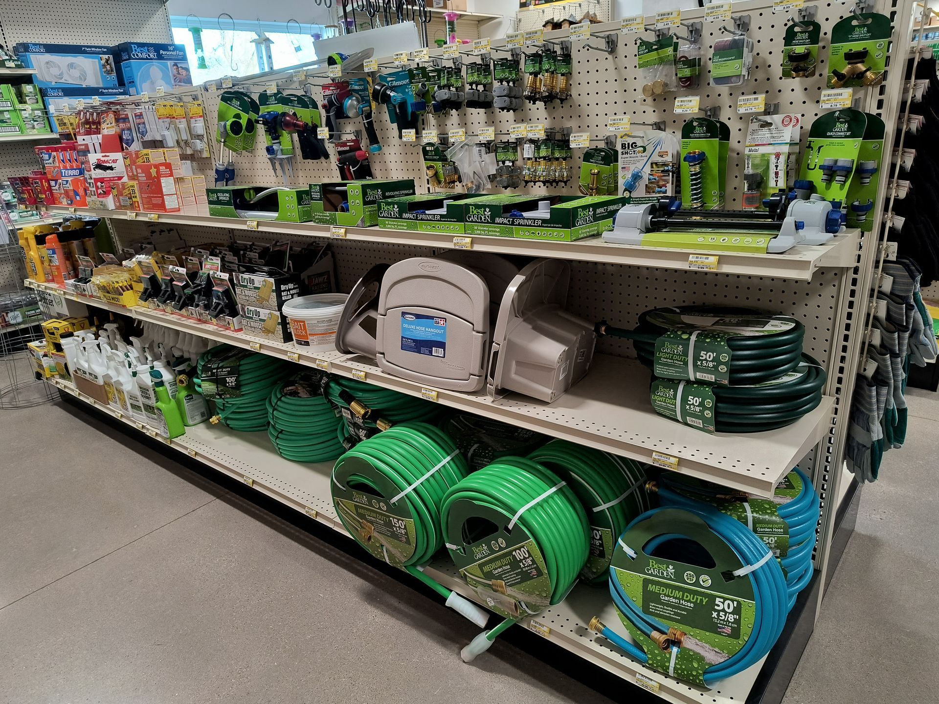 Shelves in a store filled with green garden hoses, tools, and accessories.