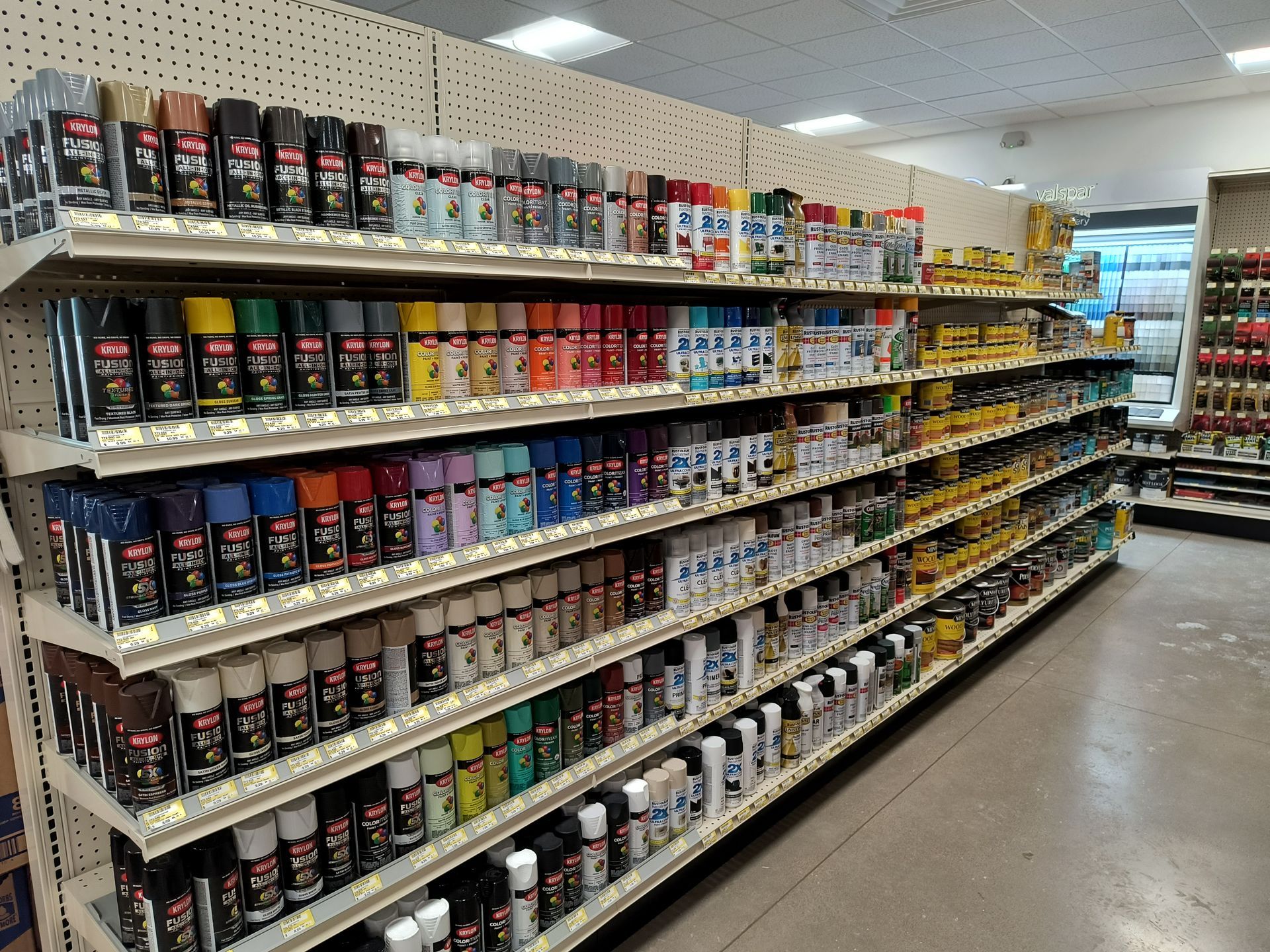 Shelves stocked with spray paint cans in various colors. Store interior, well-lit.