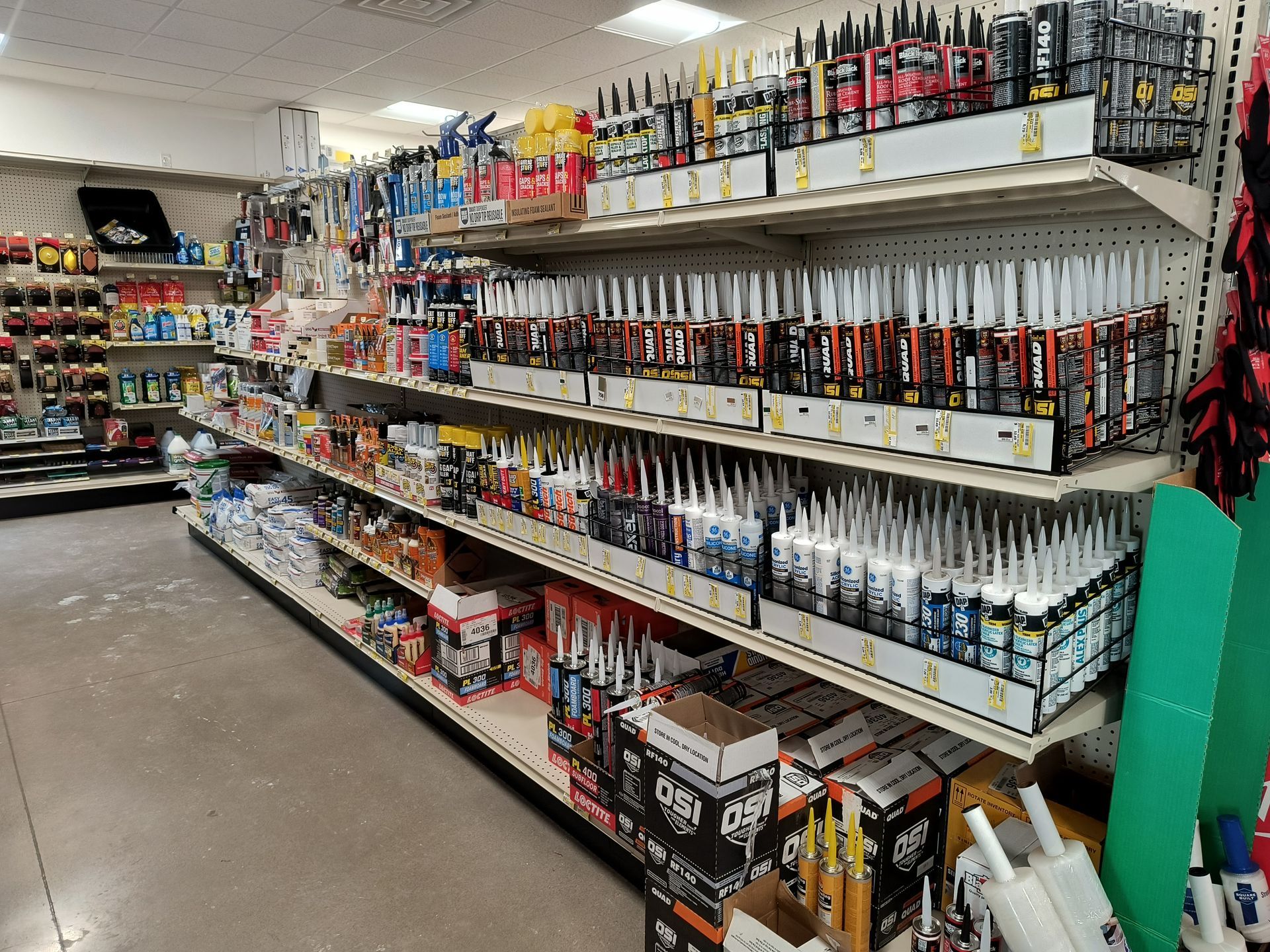 Shelves stocked with tubes of caulk and other hardware supplies in a store aisle.