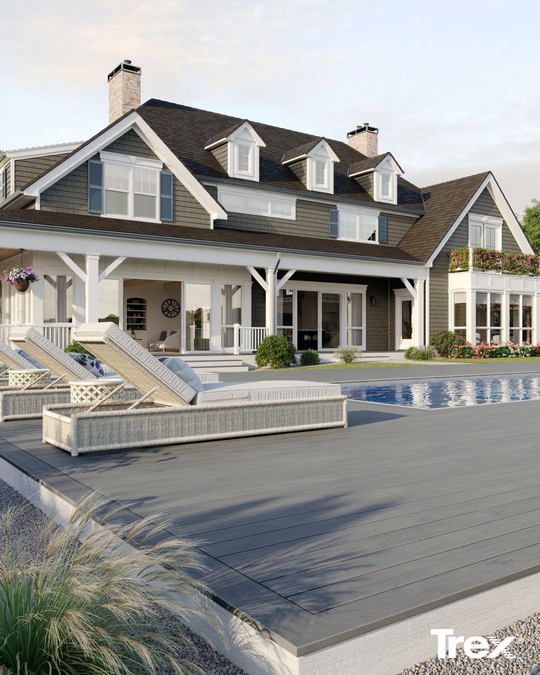 A grey Trex deck with two lounge chairs by a swimming pool, next to a large grey house with a white porch.