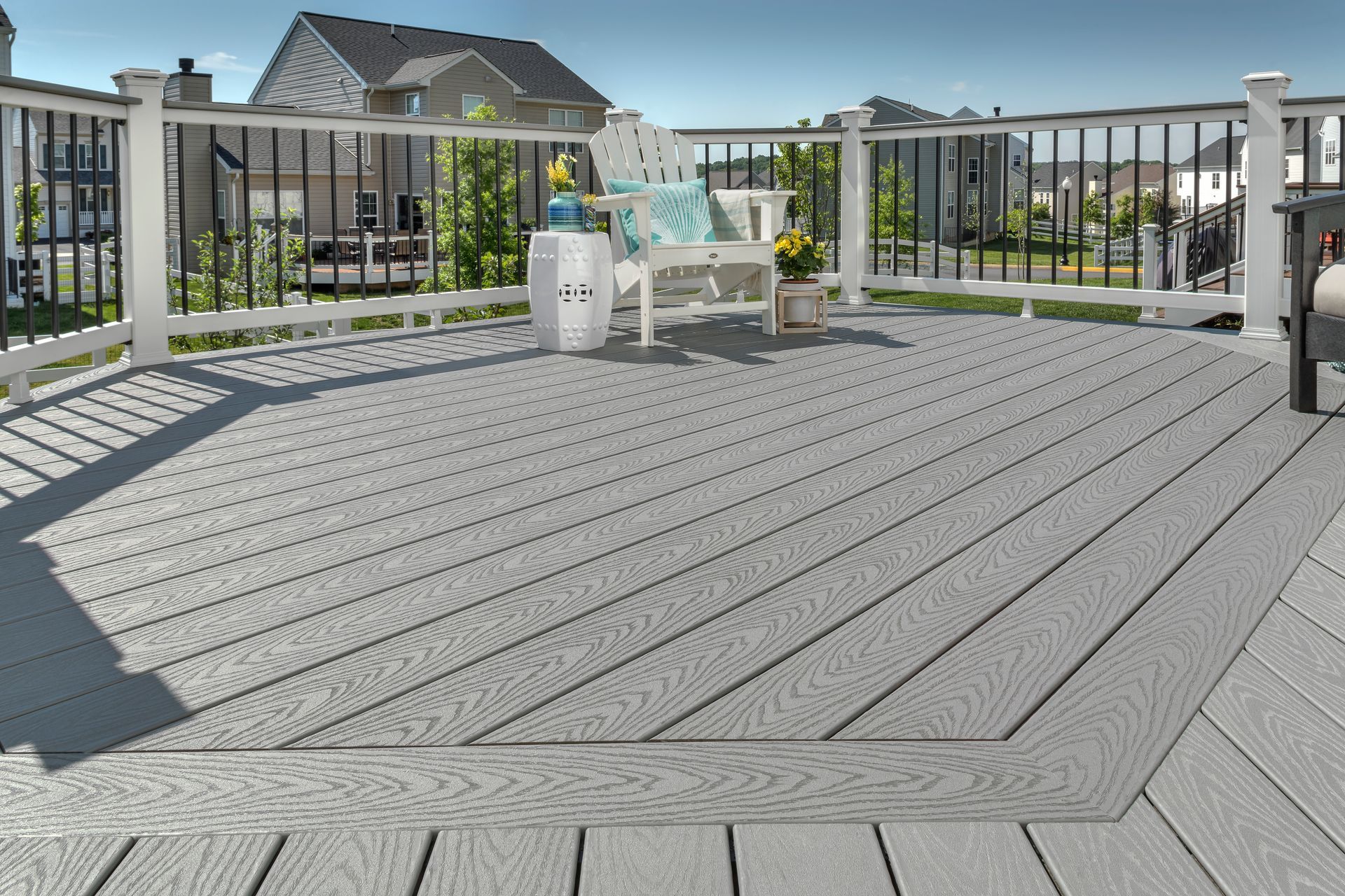 A spacious grey composite deck with a white railing and a single Adirondack chair, set in a sunny residential backyard.