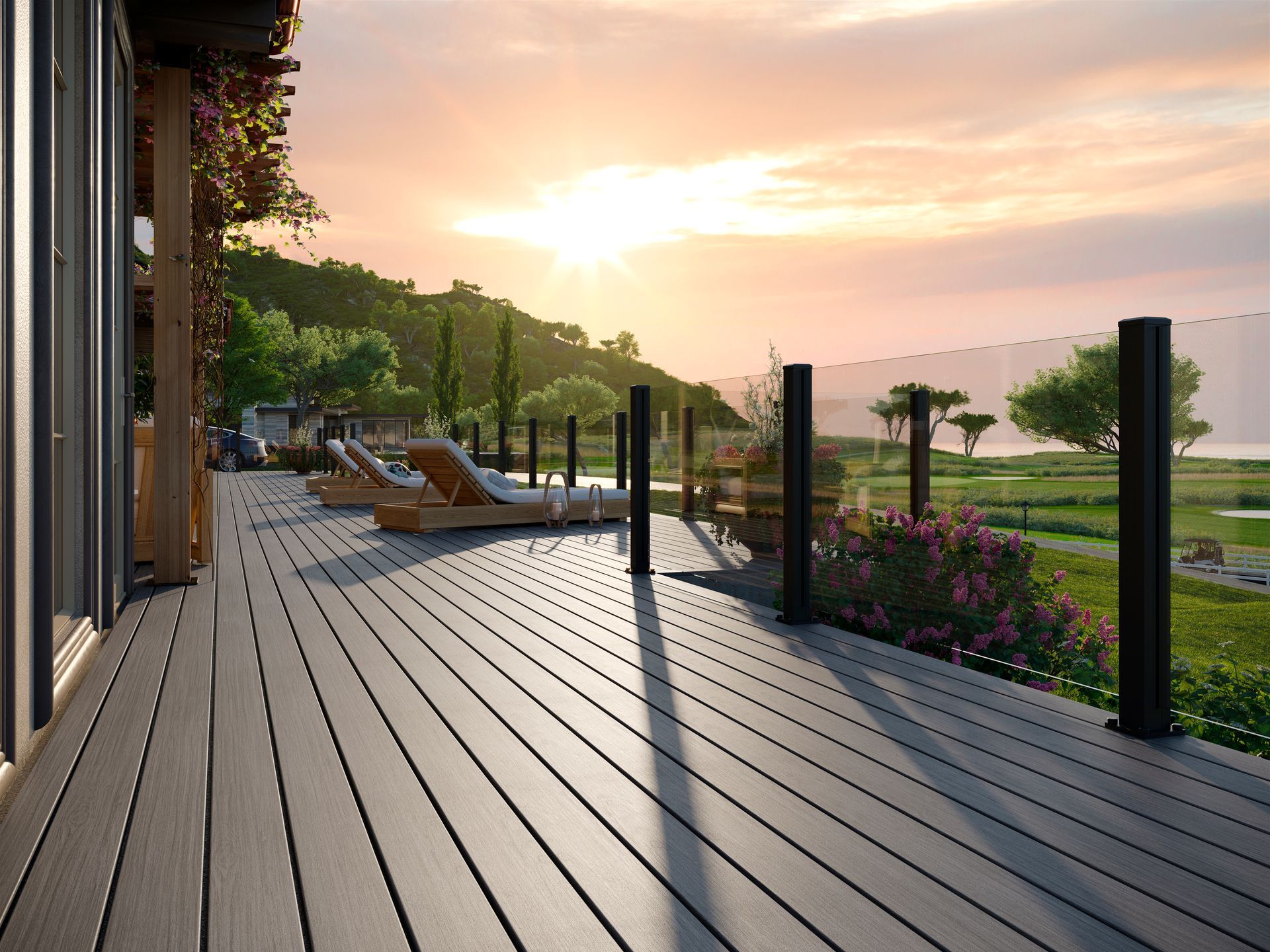 A wooden deck with black railings overlooks a lush green landscape at sunset.