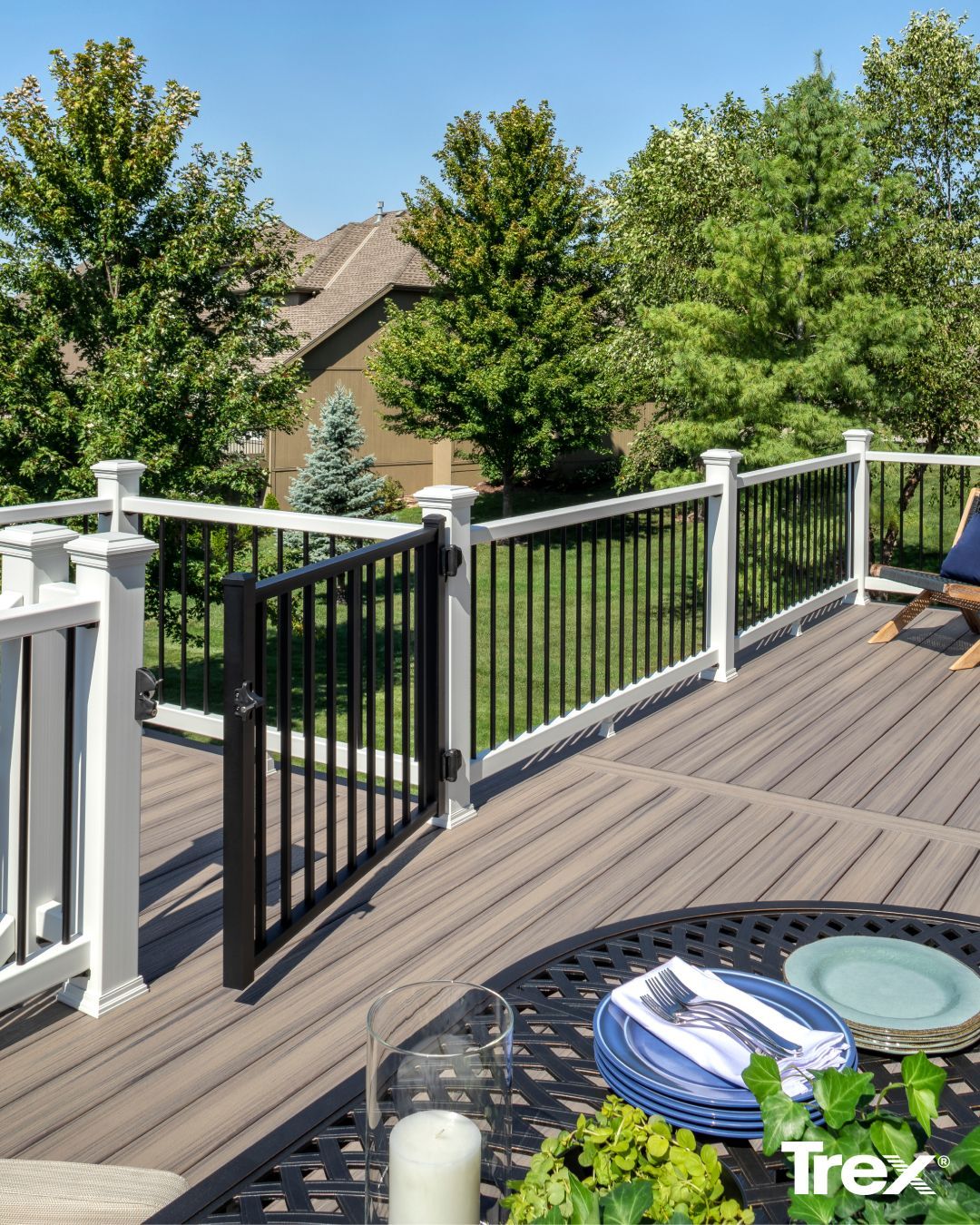 A gray composite deck with a black metal gate and railing, overlooking a lush green yard on a sunny day.