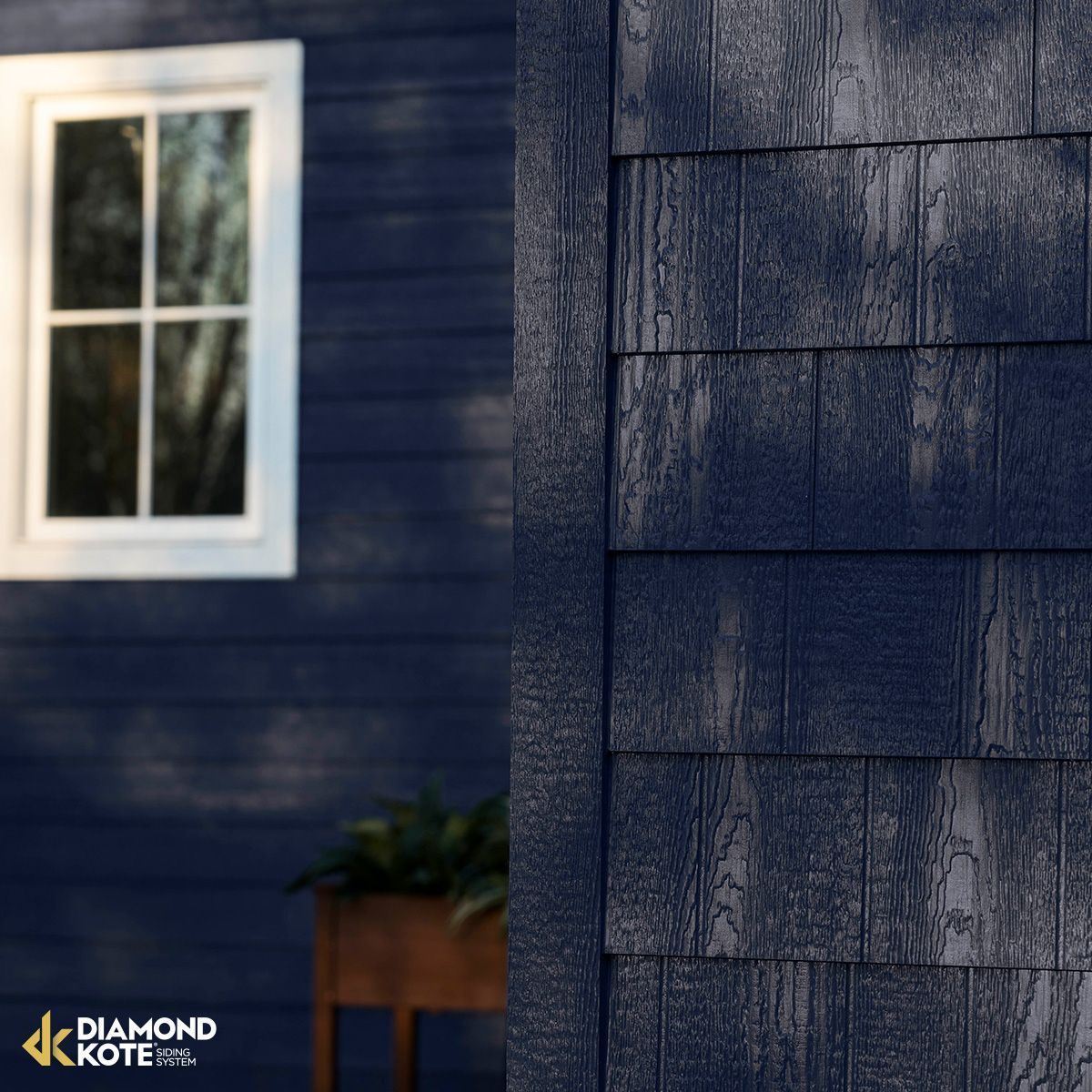 Blue house siding with a white window beside dark gray shingle siding, with a small planter below.