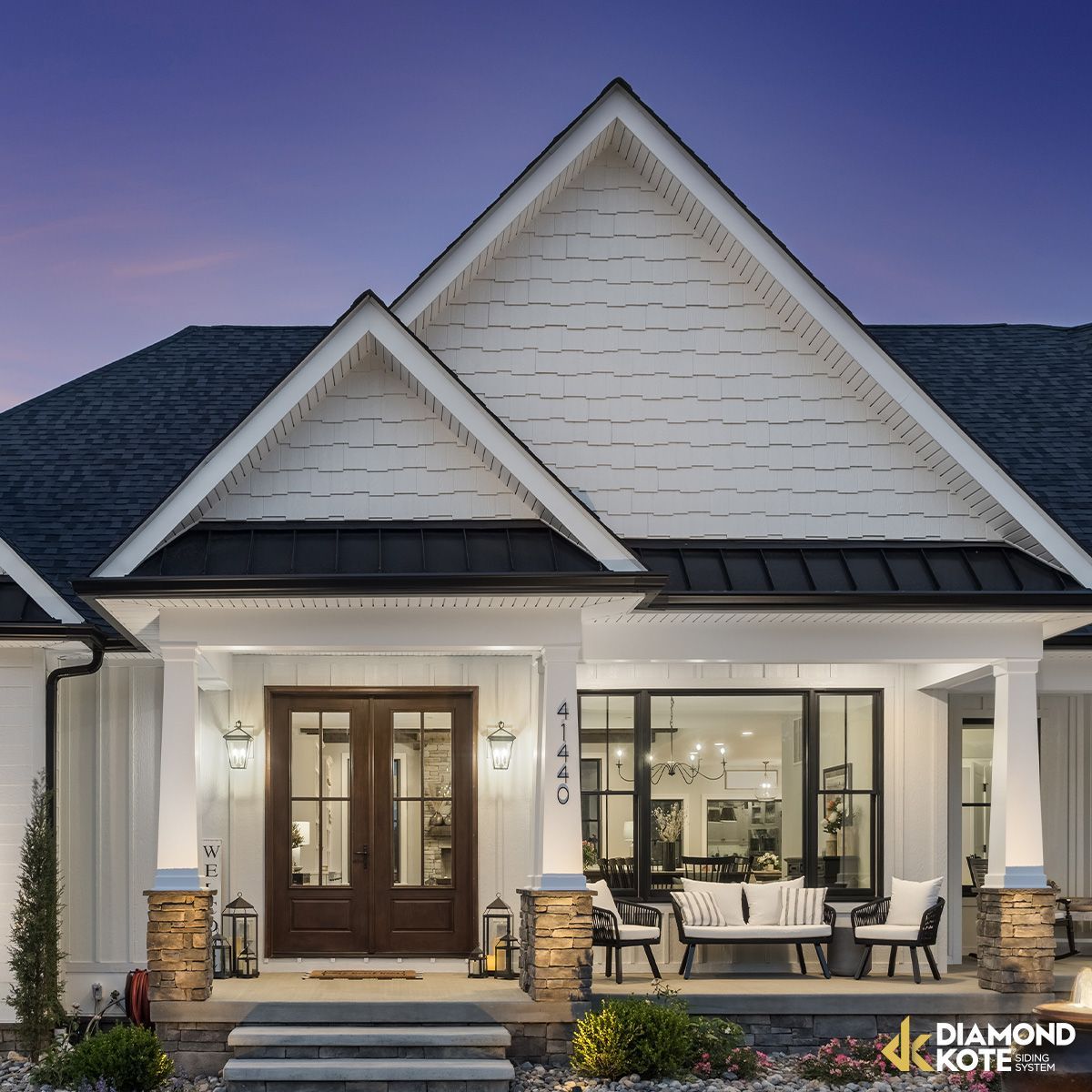 Modern white house exterior with peaked roof, front porch, and warm interior lights at dusk