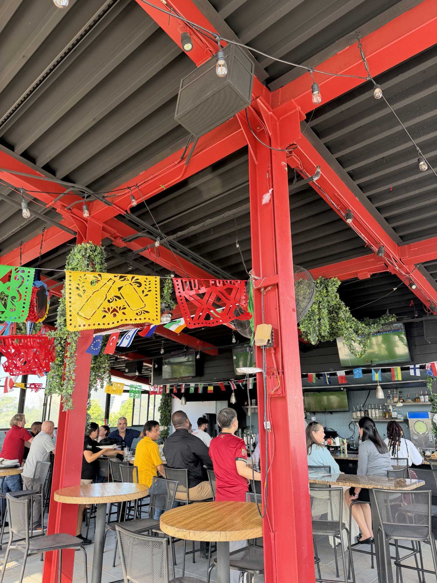 Open-air restaurant with red steel beams, hanging decorations, and people seated at tables