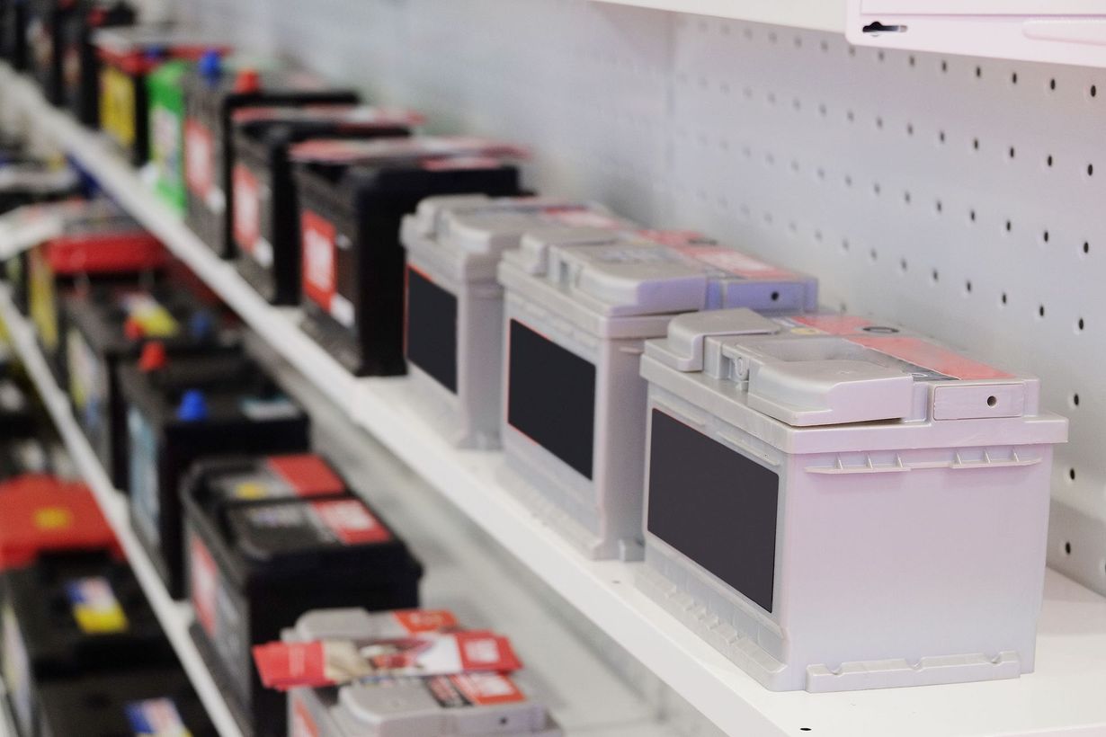 Car batteries on a shelf in a store, various colors and sizes.