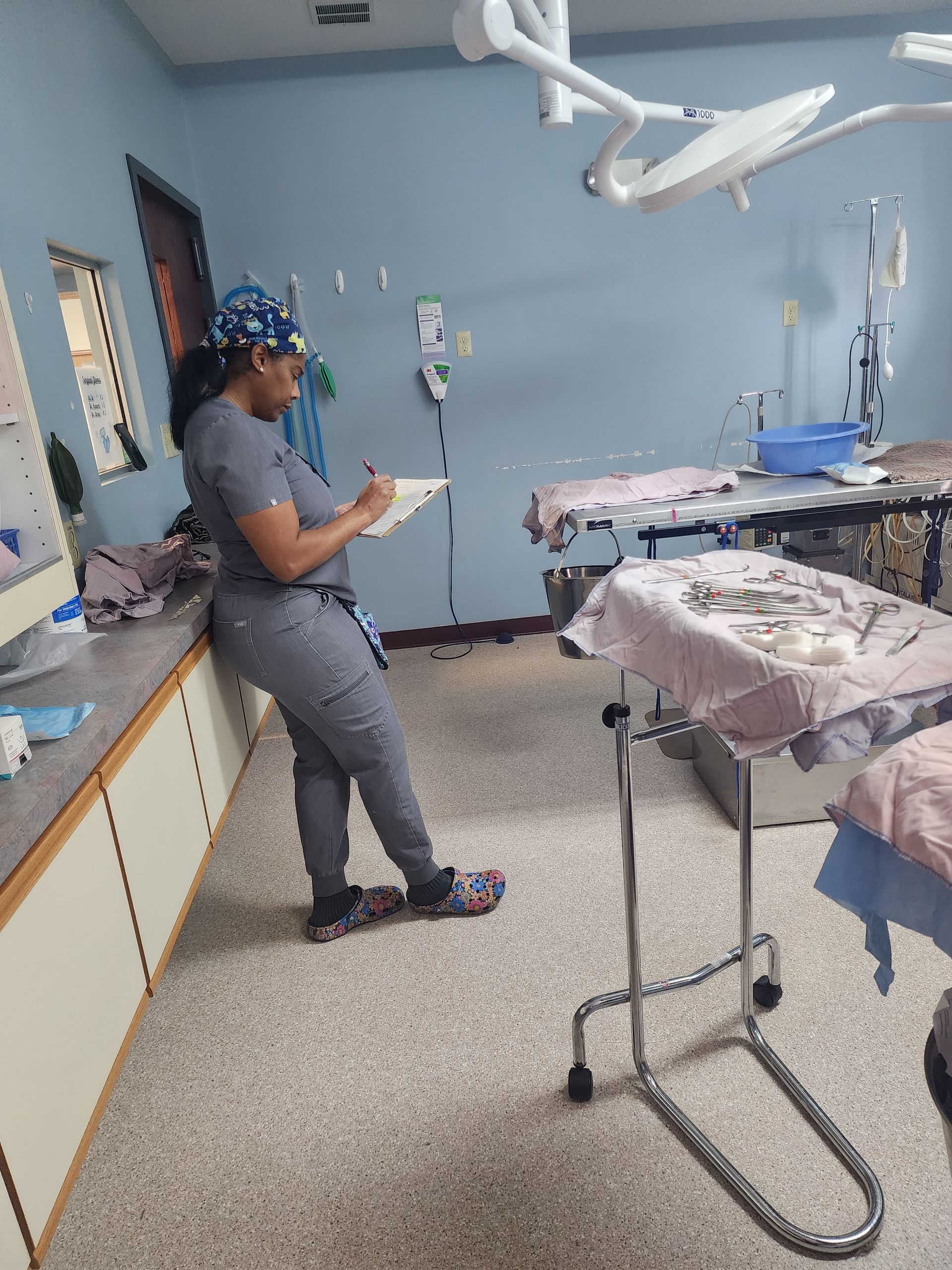 A woman is standing in an operating room writing on a clipboard.