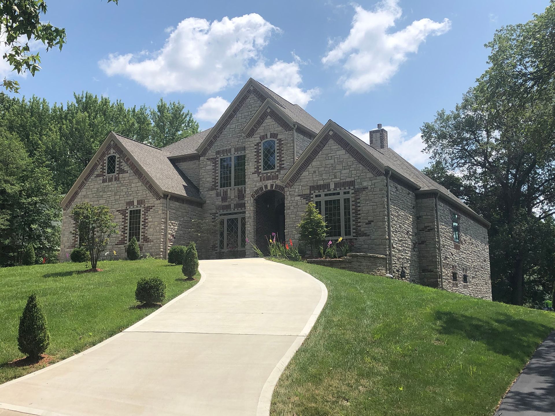A large stone house with a concrete driveway leading to it.