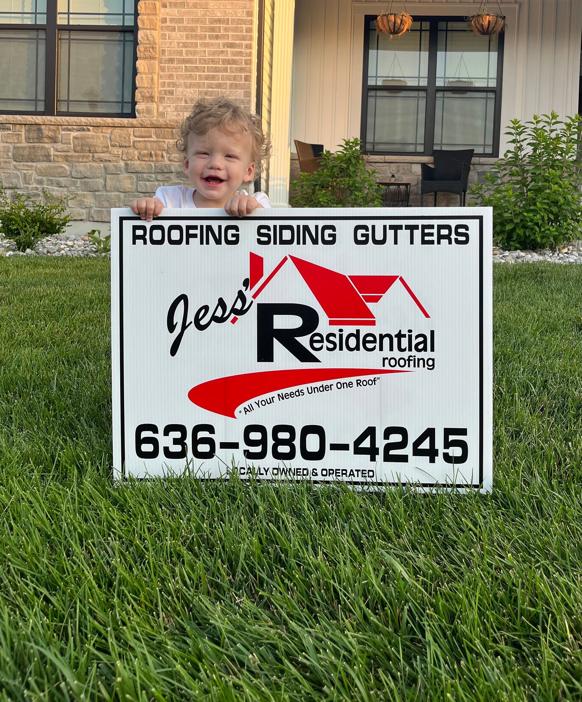 A little boy is standing in front of a sign that says roofing siding gutters.