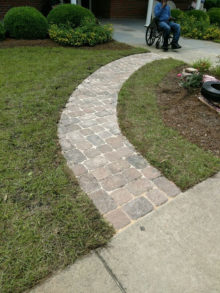 Brick pathway curving through grass, leading to a person in a wheelchair.