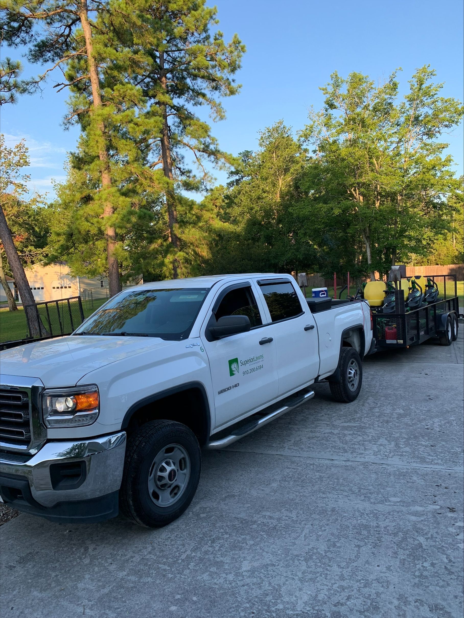 White truck with trailer, parked on gravel. Truck has logo on door. Forest background.