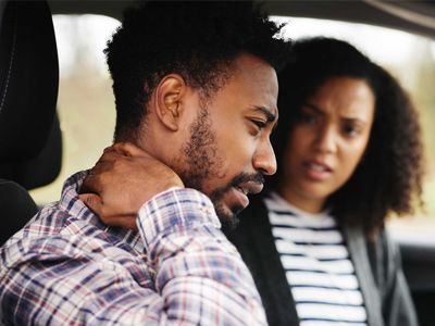 a man is sitting in the back seat of a car holding his neck.