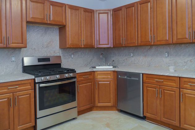 Modern kitchen with wooden cabinets, stainless steel stove and dishwasher, and light countertops.